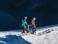 Dwóch alpinistów z rakami i czekanami wspina się po ośnieżonym zboczu.