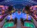 Wnętrze hotelu z basenami termalnymi, palmami i podświetlanym barem w wodzie. Relaks w tropikalnym klimacie.