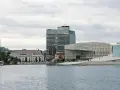 Nowoczesna architektura nad wodą, idealne miejsce, by zobaczyć, co robic w Oslo. W tle wysokie budynki i zabytkowe kamienice.