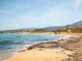 Piękne plaże Krety z turkusową wodą i piaszczystym brzegiem, w tle hotele i góry.