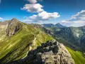 Widok na szlak prowadzący na Kasprowy Wierch. Zielone zbocza, skaliste szczyty i błękitne niebo z chmurami.