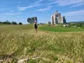 Kobieta w kapeluszu idzie przez łąkę w kierunku ruin zamku na Szlaku Orlich Gniazd.