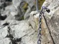 Łańcuch ułatwiający wejście na Giewont, przytwierdzony do skalnej ściany. Widok na kamienisty szlak.