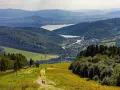 Widok na góry, jezioro i miasteczko. Turyści idą ścieżką, myśląc, gdzie w góry pociągiem wybrać się na wycieczkę.