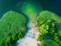 Letnie orzeźwienie nad jednym z najpiękniejszych jezior na południu Polski. Ludzie kąpią się, plażują, a łódka czeka przy brzegu.