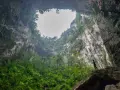 Niesamowity widok z wnętrza jaskini Hang Son Doong. Człowiek stoi na skale, podziwiając bujną roślinność i ogromne skalne ściany.