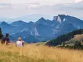Para odpoczywa na trawiastym zboczu, podziwiając malownicze góry w okolicy Szczawnicy. W oddali widać skaliste szczyty i zielone doliny.