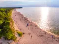 Piękna plaża nad Bałtykiem, idealna na fajne i tanie miejsca na wakacje w Polsce. Słońce odbija się w wodzie, a las tworzy malownicze tło.