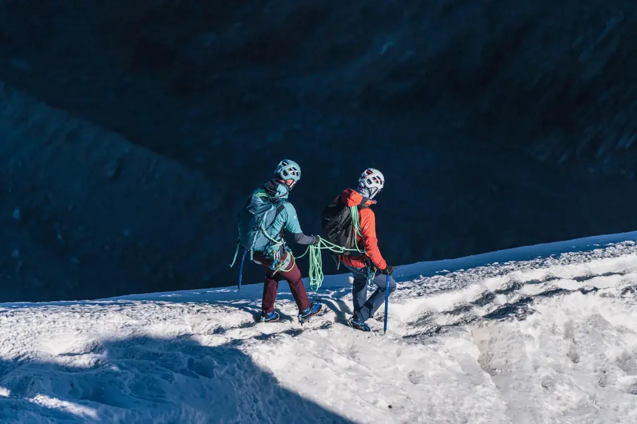 Dwóch alpinistów z rakami i czekanami wspina się po ośnieżonym zboczu.
