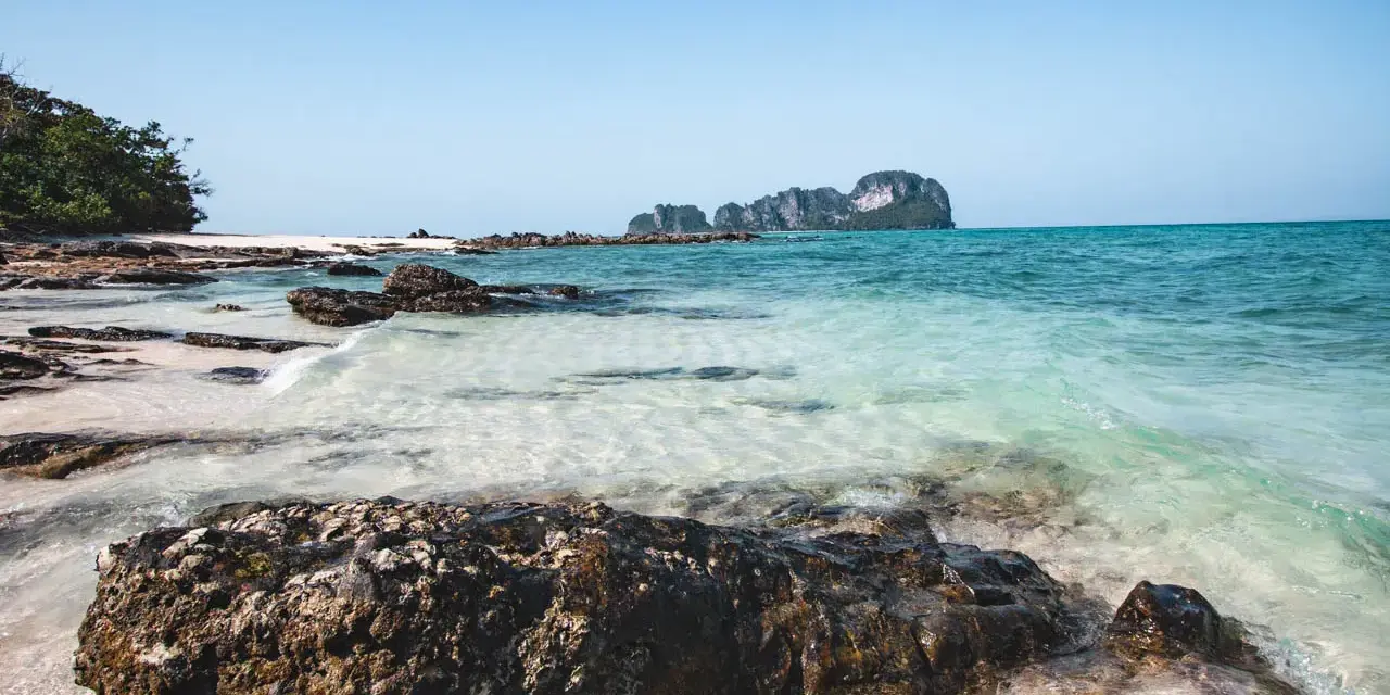 Piękne plaże i turkusowa woda, idealne miejsca w Krabi, co zobaczyć. Skały i zieleń na tle błękitnego nieba.