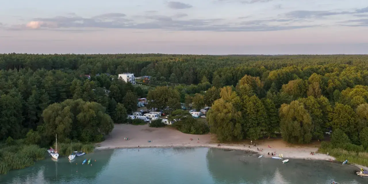 Plaża nad najczystszym jeziorem w Polsce. Woda jest turkusowa, a na brzegu widać łodzie, kajaki i ludzi odpoczywających na piasku.