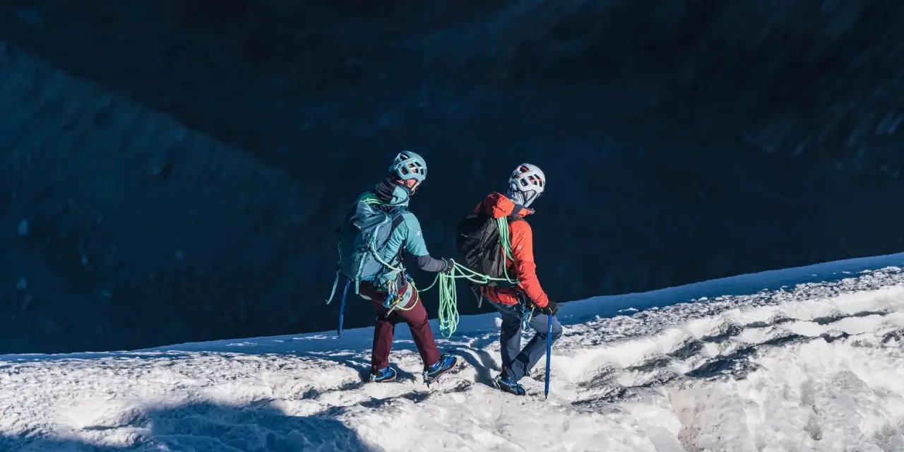 Dwóch alpinistów z rakami i czekanami wspina się po ośnieżonym zboczu.