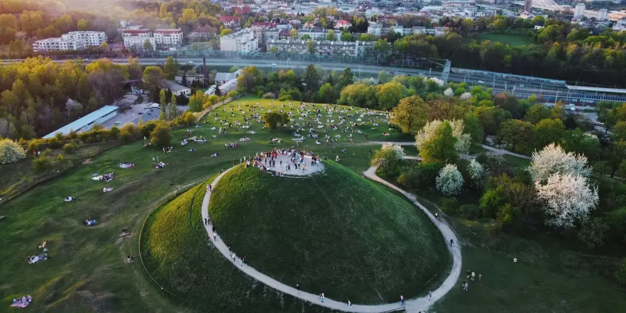 Kraków nietypowe atrakcje: Kopiec Krakusa z ludźmi na szczycie i piknikującymi na trawie. W tle rozciąga się panorama miasta.