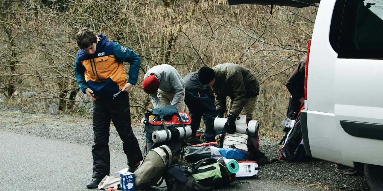 Przygotowania do wyprawy w **Tatry w Polsce**. Grupa ludzi pakuje sprzęt turystyczny przy otwartym bagażniku białego vana.