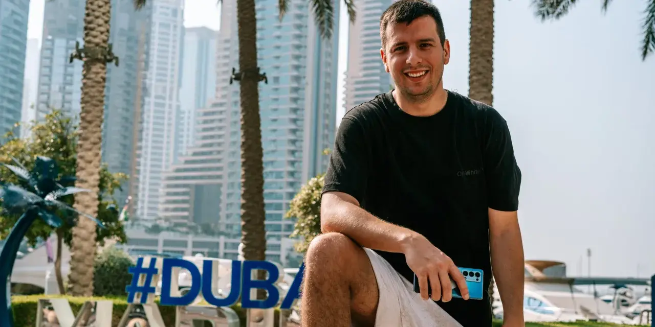 Uśmiechnięty mężczyzna z telefonem w dłoni na tle Dubaju. #Dubaj co warto wiedzieć, to świetny kierunek na wakacje.