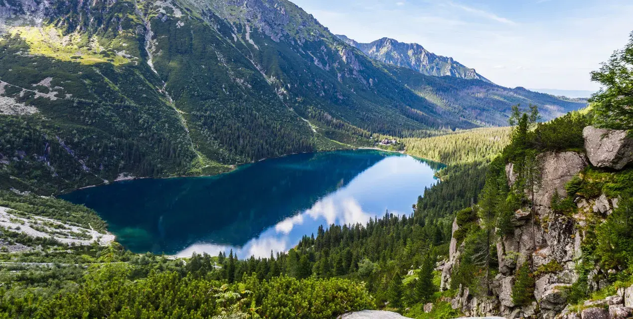 Widok na Morskie Oko, perłę polskich gór Tatr. Lśniąca tafla jeziora odbija błękitne niebo i otaczające je szczyty.
