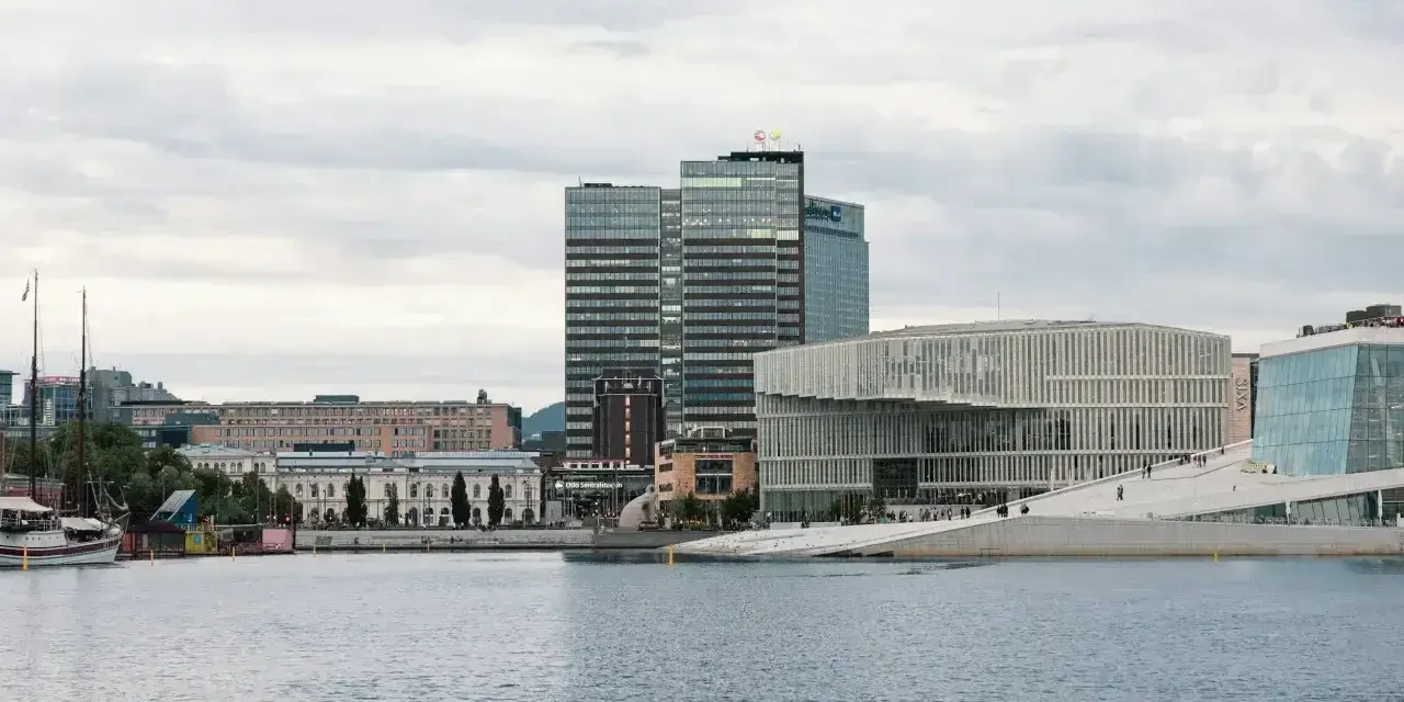 Nowoczesna architektura nad wodą, idealne miejsce, by zobaczyć, co robic w Oslo. W tle wysokie budynki i zabytkowe kamienice.