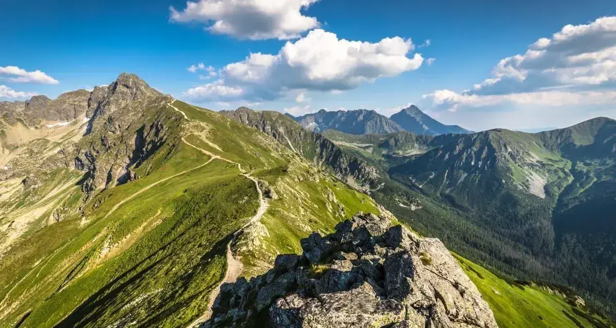 Widok na szlak prowadzący na Kasprowy Wierch. Zielone zbocza, skaliste szczyty i błękitne niebo z chmurami.