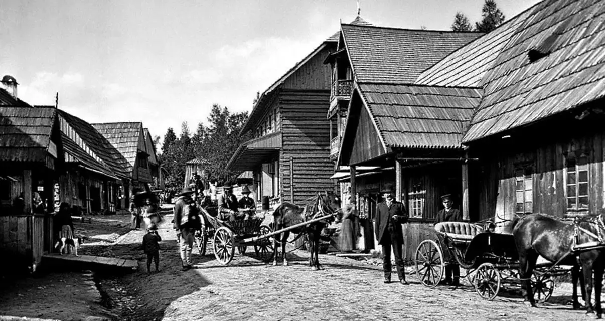 Ulica Kościeliska w Zakopanem, z drewnianymi domami i ludźmi w tradycyjnych strojach, powozy konne.