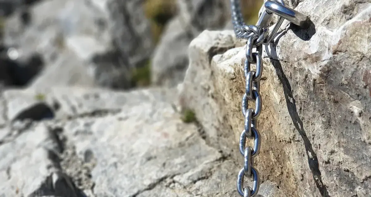 Łańcuch ułatwiający wejście na Giewont, przytwierdzony do skalnej ściany. Widok na kamienisty szlak.