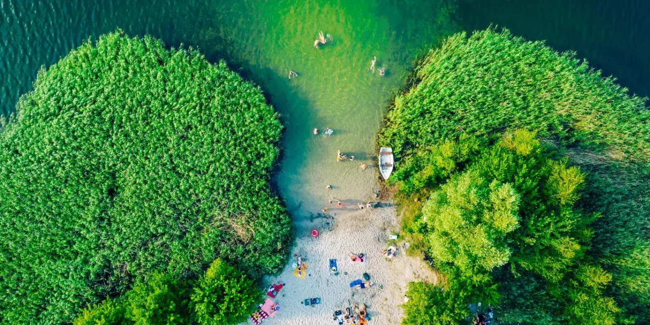 Letnie orzeźwienie nad jednym z najpiękniejszych jezior na południu Polski. Ludzie kąpią się, plażują, a łódka czeka przy brzegu.