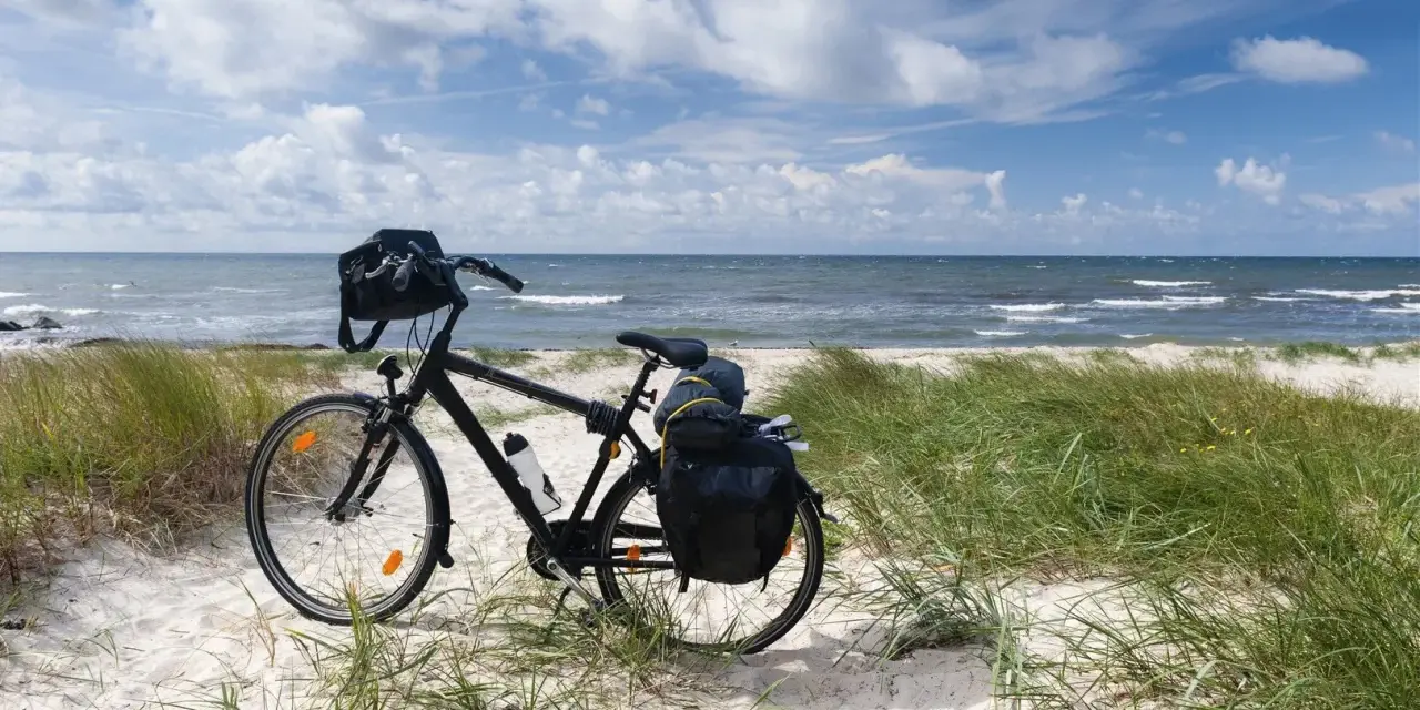 Rower z sakwami gotowy na przygodę. Trasa rowerowa wzdłuż Bałtyku zapowiada się wspaniale, z piaszczystą plażą i szumem fal.