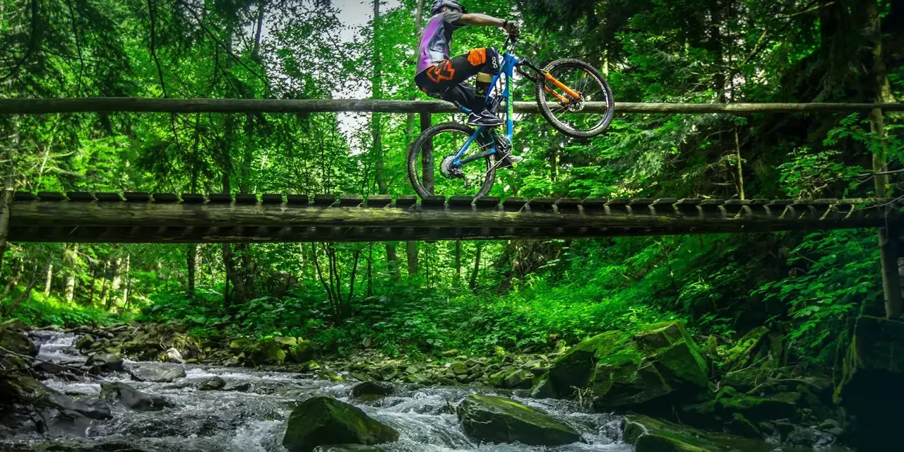 Rowerzysta wykonuje trik na drewnianym moście nad górskim potokiem. Niesamowite trasy rowerowe Zakopane czekają na odkrycie!