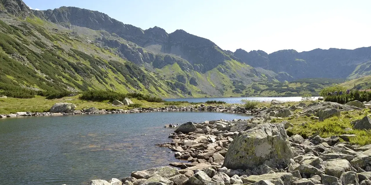 Malownicze jezioro w Tatrach, idealne na szlaki turystyczne Zakopane. Kamieniste brzegi i zielone zbocza gór tworzą piękny krajobraz.