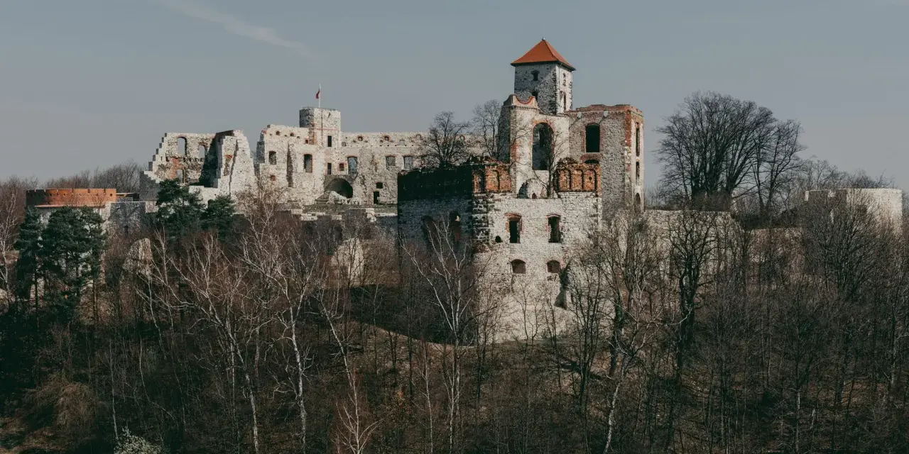 Ruiny zamku na wapiennym wzgórzu, część Szlaku Orlich Gniazd, otoczone drzewami.
