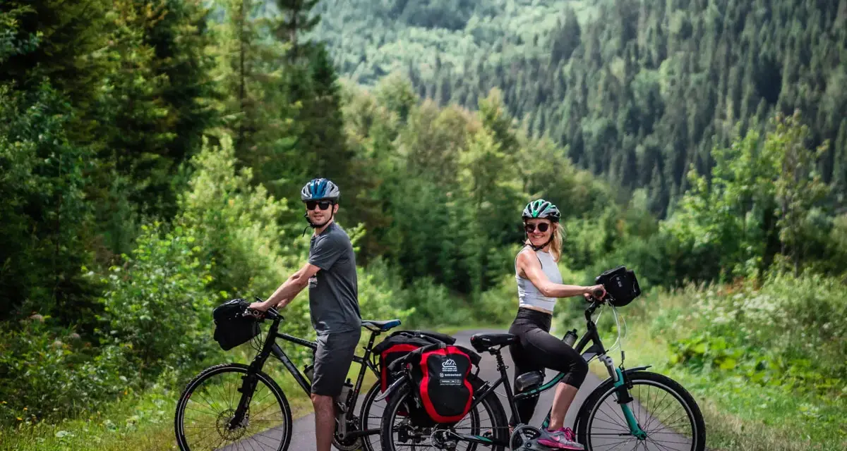 Para rowerzystów na tle górskiego lasu, gotowa na odkrywanie tras rowerowych Tatr.