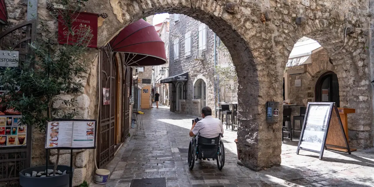 Mężczyzna na wózku inwalidzkim przemierza urokliwe uliczki budva stare miasto, podziwiając kamienne łuki i zabytkową architekturę.