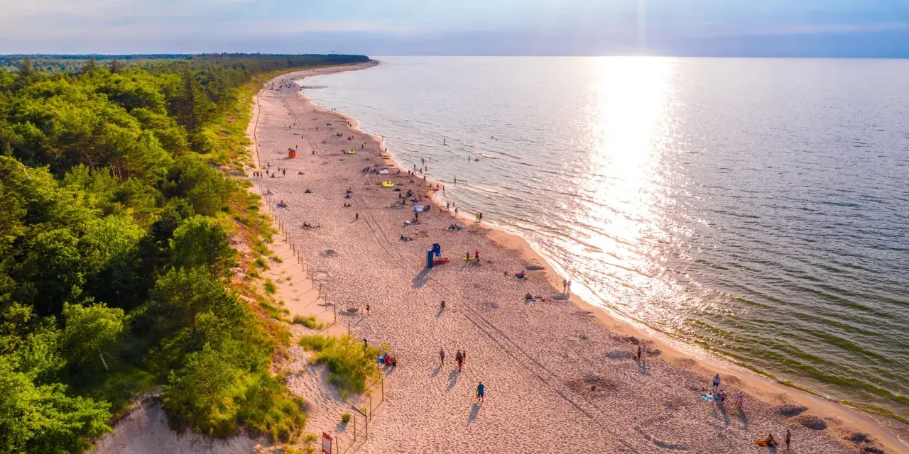 Piękna plaża nad Bałtykiem, idealna na fajne i tanie miejsca na wakacje w Polsce. Słońce odbija się w wodzie, a las tworzy malownicze tło.