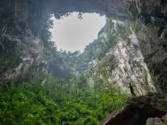Niesamowity widok z wnętrza jaskini Hang Son Doong. Człowiek stoi na skale, podziwiając bujną roślinność i ogromne skalne ściany.