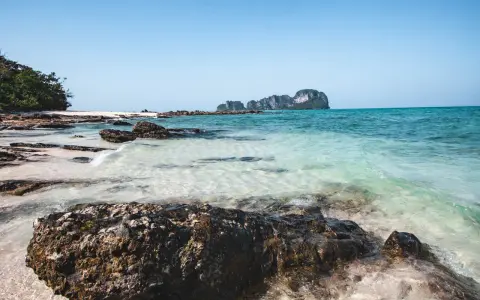Piękne plaże i turkusowa woda, idealne miejsca w Krabi, co zobaczyć. Skały i zieleń na tle błękitnego nieba.