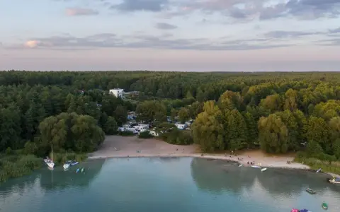 Plaża nad najczystszym jeziorem w Polsce. Woda jest turkusowa, a na brzegu widać łodzie, kajaki i ludzi odpoczywających na piasku.