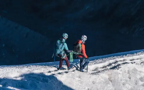 Dwóch alpinistów z rakami i czekanami wspina się po ośnieżonym zboczu.