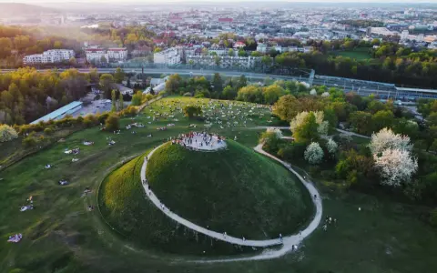 Kraków nietypowe atrakcje: Kopiec Krakusa z ludźmi na szczycie i piknikującymi na trawie. W tle rozciąga się panorama miasta.