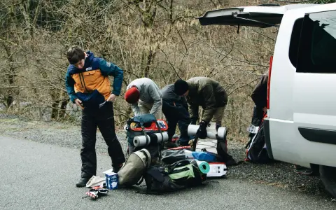 Przygotowania do wyprawy w **Tatry w Polsce**. Grupa ludzi pakuje sprzęt turystyczny przy otwartym bagażniku białego vana.