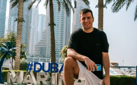 Uśmiechnięty mężczyzna z telefonem w dłoni na tle Dubaju. #Dubaj co warto wiedzieć, to świetny kierunek na wakacje.