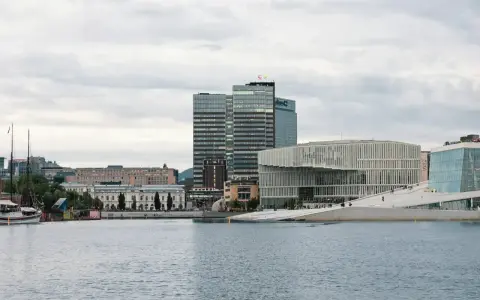 Nowoczesna architektura nad wodą, idealne miejsce, by zobaczyć, co robic w Oslo. W tle wysokie budynki i zabytkowe kamienice.