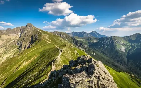 Widok na szlak prowadzący na Kasprowy Wierch. Zielone zbocza, skaliste szczyty i błękitne niebo z chmurami.