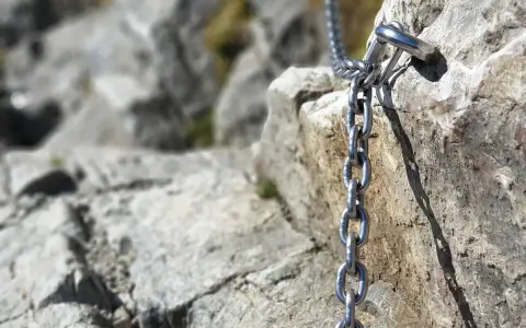 Łańcuch ułatwiający wejście na Giewont, przytwierdzony do skalnej ściany. Widok na kamienisty szlak.
