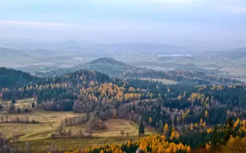 Jesienny krajobraz z kolorowymi drzewami na tle mglistych, niskich gór w Polsce.