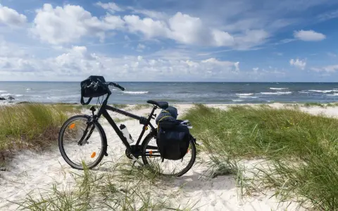Rower z sakwami gotowy na przygodę. Trasa rowerowa wzdłuż Bałtyku zapowiada się wspaniale, z piaszczystą plażą i szumem fal.