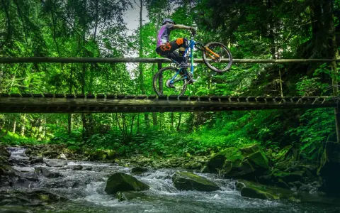 Rowerzysta wykonuje trik na drewnianym moście nad górskim potokiem. Niesamowite trasy rowerowe Zakopane czekają na odkrycie!