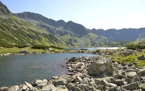 Malownicze jezioro w Tatrach, idealne na szlaki turystyczne Zakopane. Kamieniste brzegi i zielone zbocza gór tworzą piękny krajobraz.