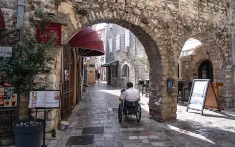 Mężczyzna na wózku inwalidzkim przemierza urokliwe uliczki budva stare miasto, podziwiając kamienne łuki i zabytkową architekturę.