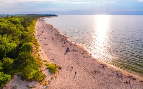 Piękna plaża nad Bałtykiem, idealna na fajne i tanie miejsca na wakacje w Polsce. Słońce odbija się w wodzie, a las tworzy malownicze tło.