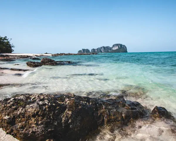 Piękne plaże i turkusowa woda, idealne miejsca w Krabi, co zobaczyć. Skały i zieleń na tle błękitnego nieba.