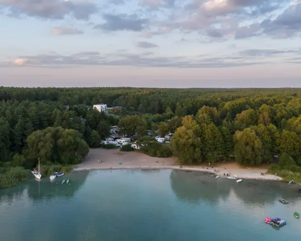 Plaża nad najczystszym jeziorem w Polsce. Woda jest turkusowa, a na brzegu widać łodzie, kajaki i ludzi odpoczywających na piasku.